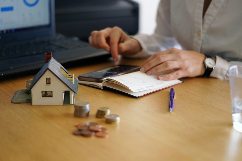 Person calculating finances with a house model and coins on the table.